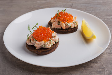 Toast skagen - classic Swedish appetizer. Sandwiches with shrimps and caviar on white plate. Nordic cuisine.