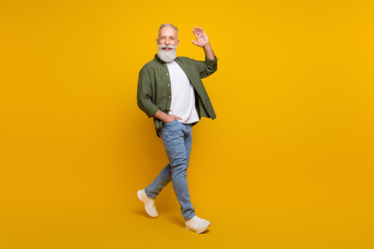 Full length body size photo of positive happy senior man smiling waving hand isolated vivid yellow color background