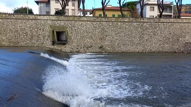 Scorcio del fiume Bisenzio a Prato in Toscana, che scorre e incontrando una piccola chiusa crea schiuma, spruzzi e onde