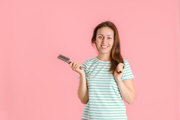 A happy brunette does her hair and smiles while holding a massage brush for her hair. Pink background