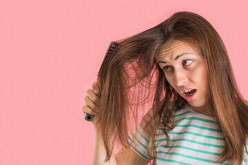 Brunette pulls a comb out of tangled hair and screams in pain, pink background