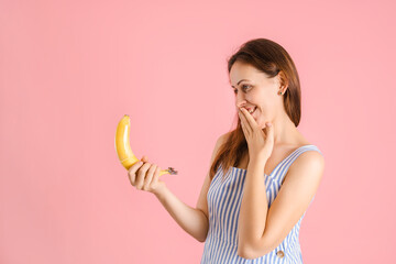 A woman holds a banana with a condom on it and shyly covers her mouth with her palm. Copy space