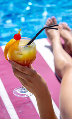 a girl on a sun lounger near the pool drinks a cocktail from a freshly squeezed orange. Recreation