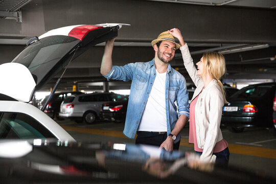 Young woman putting trilby on boyfriend's head in airport parking lot