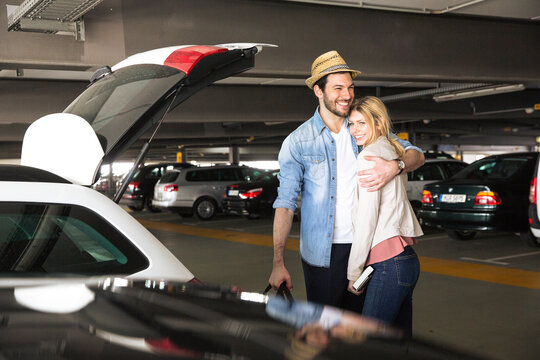 Smiling man embracing girlfriend in airport parking lot