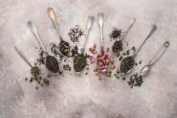 Dry tea in a spoon. Green, black, herbal and flower teas. Brown grunge background. Top view, flat...