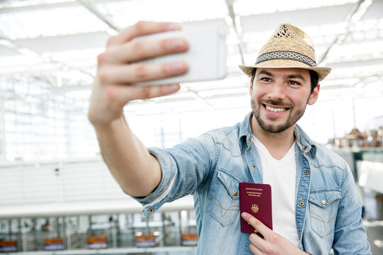 Young man holding passport while taking selfie in airport departure area