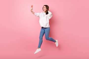 Fototapeta na wymiar Photo of funny cute young woman dressed white sweatshirt tacking selfie jumping high smiling isolated pink color background