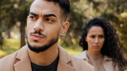 Close-up young serious disgruntled man in background offended angry upset woman hispanic couple...