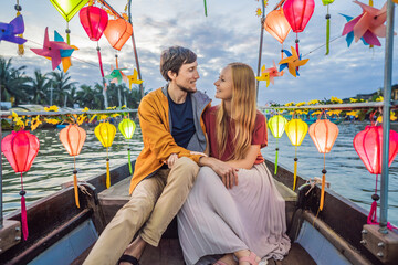 Happy couple of travelers ride a national boat on background of Hoi An ancient town, Vietnam. Vietnam opens to tourists again after quarantine Coronovirus COVID 19
