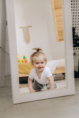 A cute baby smiles and crawls on the floor near the mirror in the house.