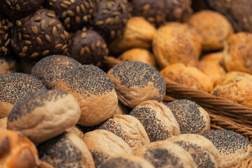 Close-up photo of breakfast lines of  rye buns with sunflower seeds and white wheat buns with poppy seeds in wooden trays at the hotel restaurant.