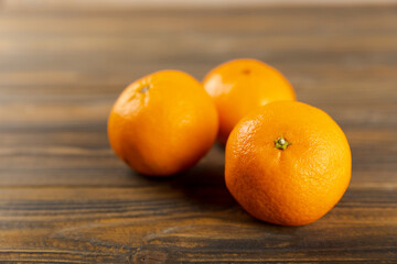Orange-colored mandarin or clementine fruits with green leaves, on a tree background.