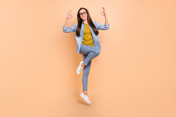 Fototapeta na wymiar Full size photo of smiling mature lady jumping showing okay sign wear spectacles isolated on beige color background