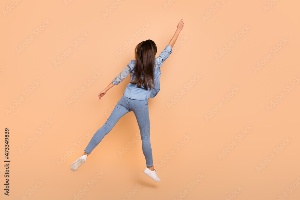 Poster full size back view photo of slim woman painting wall jumping fooling around isolated on beige color