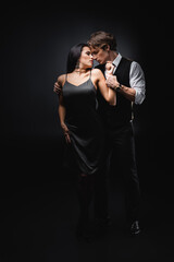 full length of man in vest and shirt hugging girlfriend in sexy slip dress on black.