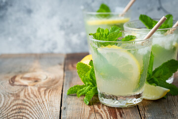 Two glass with lemonade or mojito cocktail with lemon and mint, cold refreshing drink or beverage with ice on rustic blue background. Copy space
