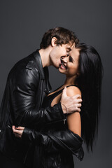 joyful and sexy couple in leather jackets laughing isolated on grey.