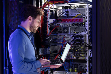 Male IT specialist working on laptop in server room