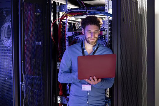 Male IT expertise using laptop in front of rack at server room