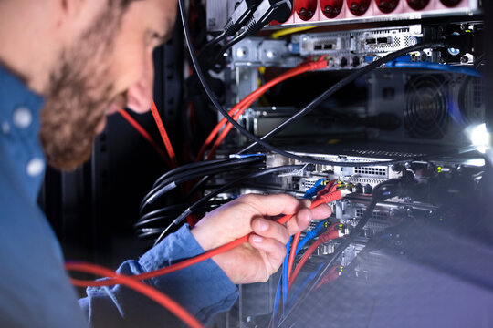 Male IT specialist installing patch cord cable in server rack in data center