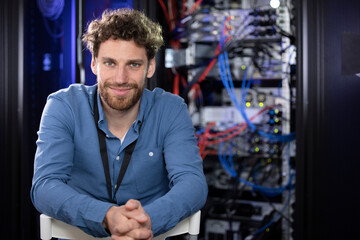 Contented male IT specialist with hands clasped sitting at data center