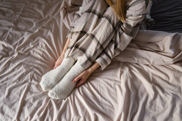 The girl lies in bed in pajamas and warm socks. Women's legs in cozy white fluffy socks in bed....