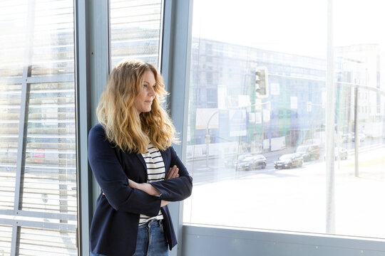 Businesswoman with arms crossed contemplating while standing by window in office