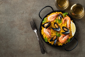 Traditional spanish seafood paella in pan with chickpeas, shrimps, mussels, squid on brown concrete background. Top view with copy space
