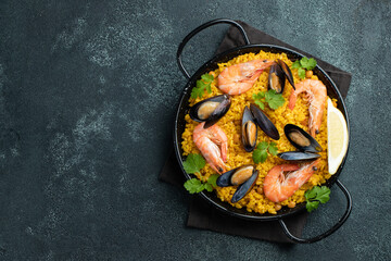 Traditional spanish seafood paella in pan with chickpeas, shrimps, mussels, squid on black concrete background. Top view with copy space
