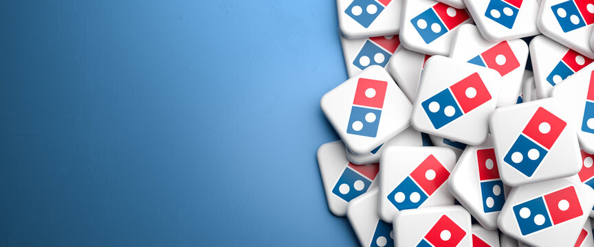 Logos of the American pizza restaurant chain Domino's Pizza on a heap on a table. Copy space. Web banner format.