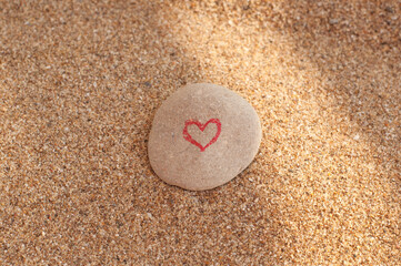 a painted red heart on a flat pebble on a sand background