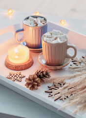 two cups of  hot drink with marshmallows  and christmas decor on white wooden tray