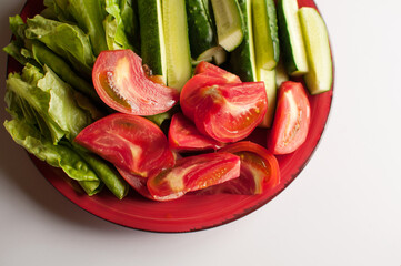 sliced tomatoes and cucumbers on a red plate on a white background