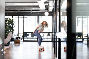 Smiling female professional doing skateboarding in office
