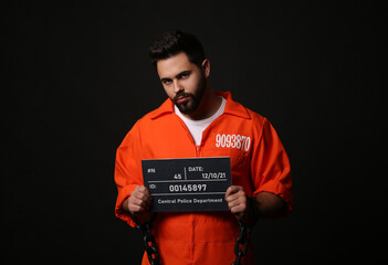 Fototapeta na wymiar Prisoner with chained hands holding mugshot letter board on black background