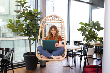Businesswoman working on laptop while sitting on swing chair at office cafeteria