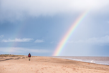 Rainbow over a beach with a man walking towards the rainbow
