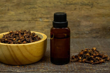 Essential oil of cloves in bottle and dry cloves on wooden bowl on rustic wooden background.
