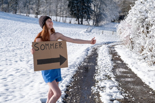 Smiling woman with sign board hitchhiking on snow covered road