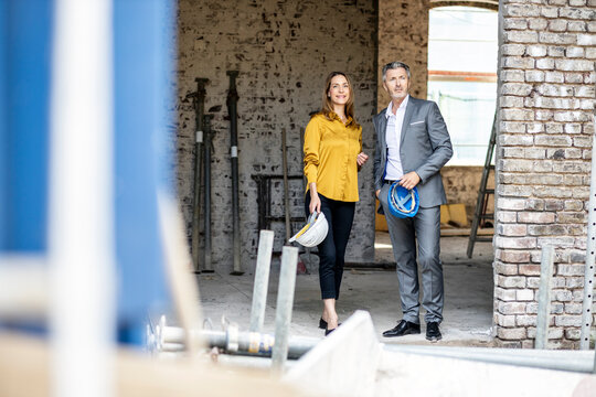 Female architect with hardhat standing with male client at construction site