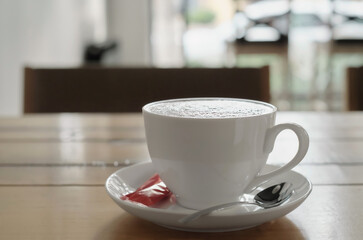 Cappuccino coffee in a white cup on a wooden table. Selective focus on a cup in a cafe with background lighting