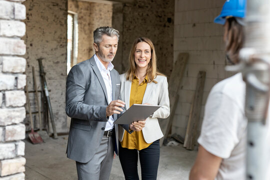 Male architect with digital tablet standing by smiling female colleague at site