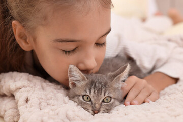 Cute little girl with kitten on white blanket, closeup. Childhood pet