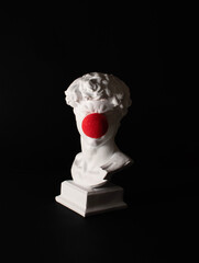 Plaster male bust with red nose ball against dark background. Minimal pop culture idea.