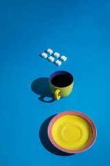 Sugar cubes, yellow a cup of coffee and a yellow-pink tray on a blue background. Great, cool and minimalistic look. 
