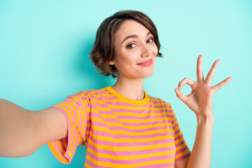 Photo of charming cute young lady wear orange t-shirt recording video showing okey smiling isolated turquoise color background