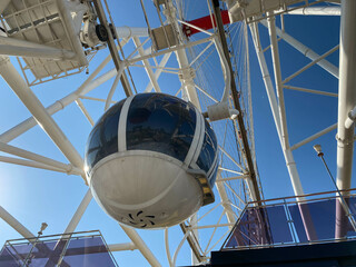 A large Ferris wheel against a blue sky. Booths with people go up