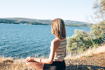 Young beautiful teenage girl meditating on the seashore and enjoys the landscape. Walk in nature in summer