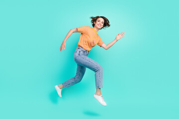 Fototapeta na wymiar Photo of impressed cute young lady wear orange t-shirt jumping high running fast smiling isolated turquoise color background